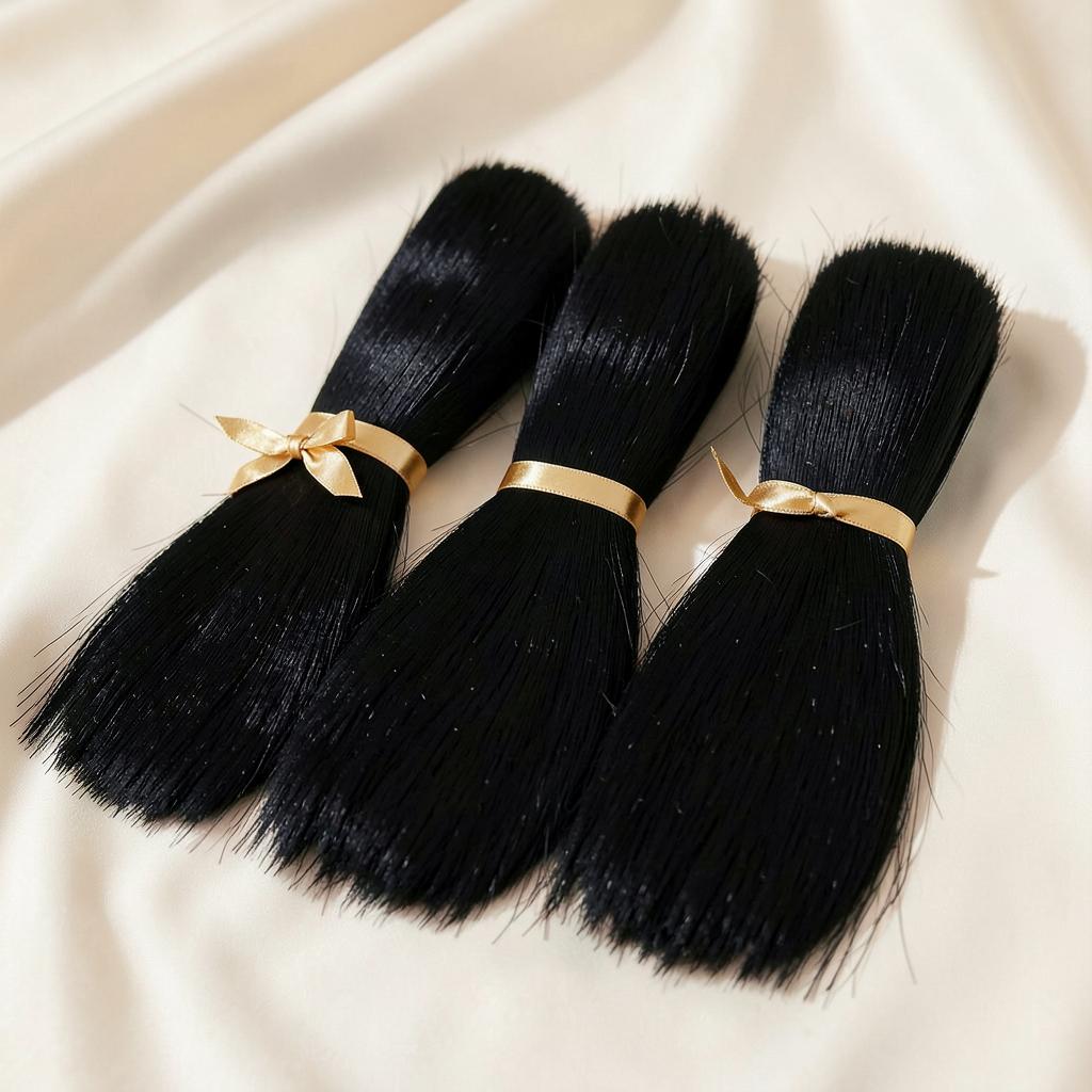 Three straight black hair extension bundles tied with gold ribbon